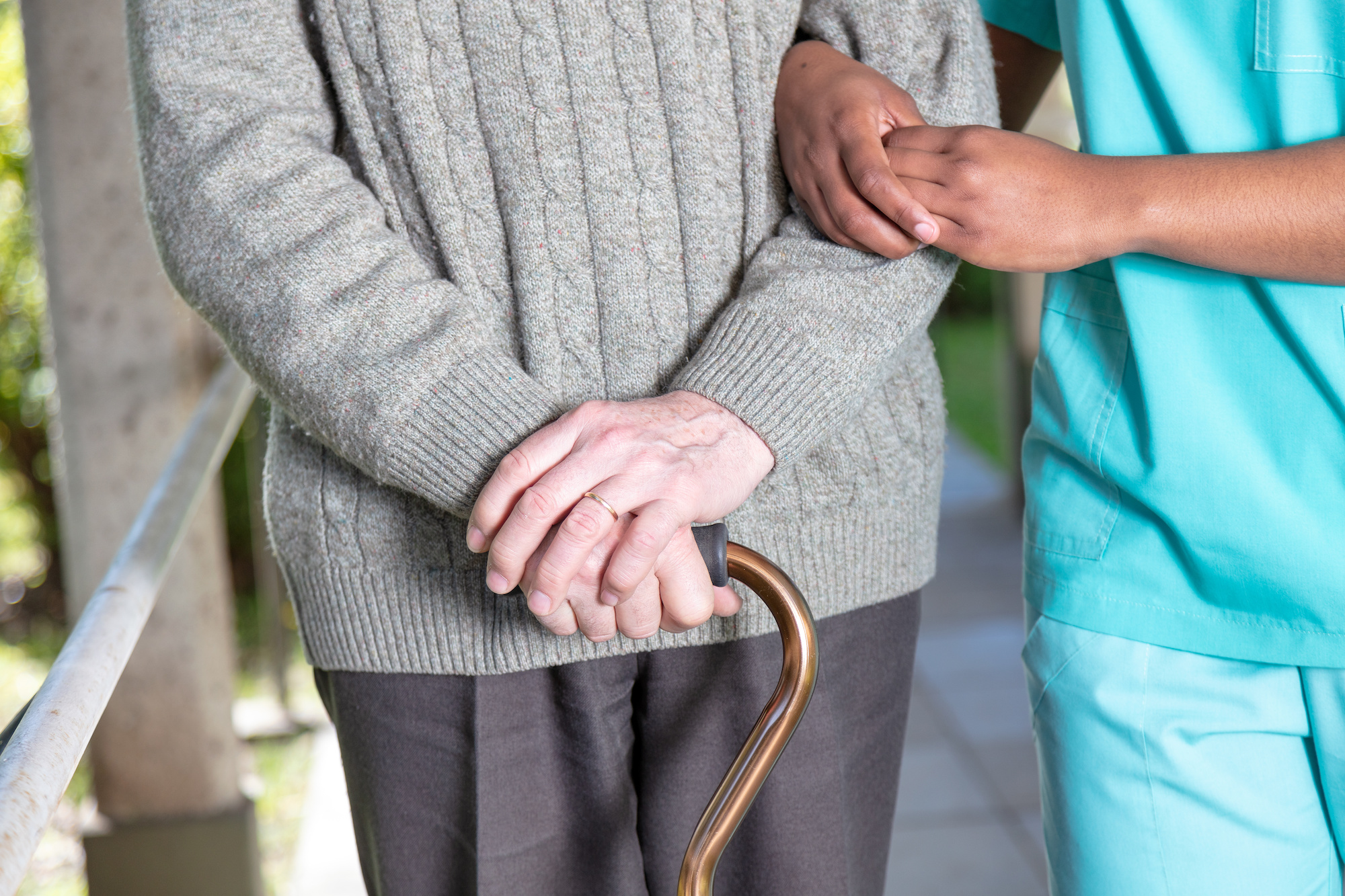 Elderly man with walking stick moving with nurse, detail on the hands